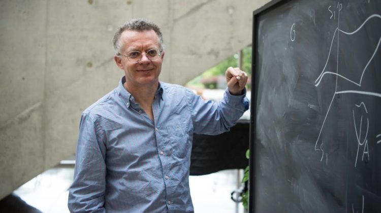physicist Lucien Hardy leans against a blackboard, chalk in hand.