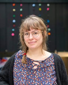 Portrait of a young woman standing in an atrium wearing a purple shirt and black cardigan