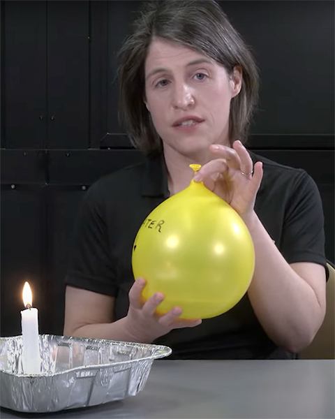 Woman wearing black shirt, doing science demonstration with balloon and lit candle