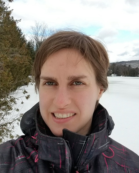 Portrait of a woman outside in winter with trees and frozen lake behind her