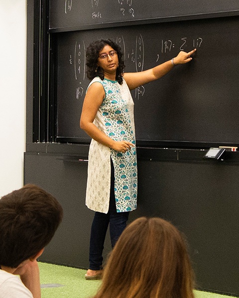 A woman with long dark hair teaches a lesson at a blackboard.