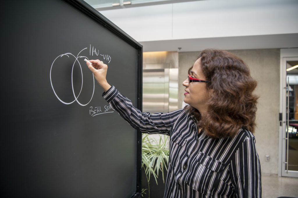 Woman in a striped blouse and brown hair working on equations at a chalkboard