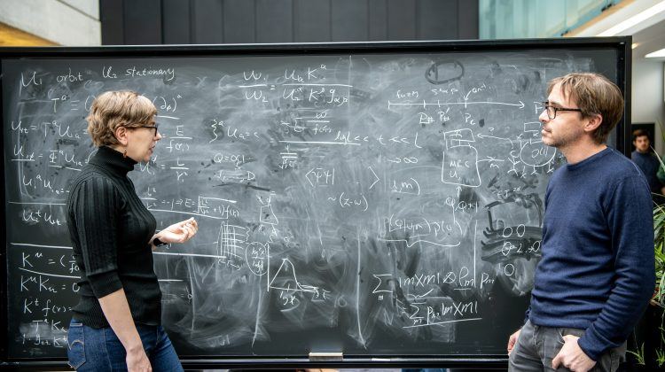 Two researchers, a woman and a man, working together at a blackboard